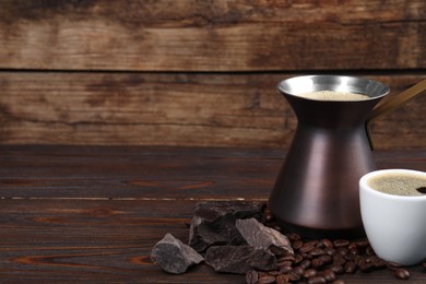 Photo of Hot turkish coffee pot, beans, cup of drink and chocolate on wooden table, space for text