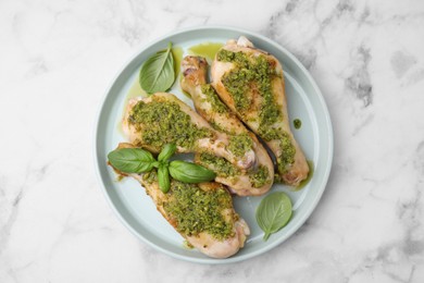 Photo of Delicious fried chicken drumsticks with pesto sauce and basil on white marble table, top view
