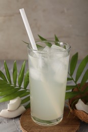 Photo of Glass of coconut water, ice cubes, leaves and nuts on grey table
