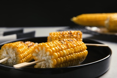 Photo of Ceramic plate with grilled corn cobs on light table, closeup