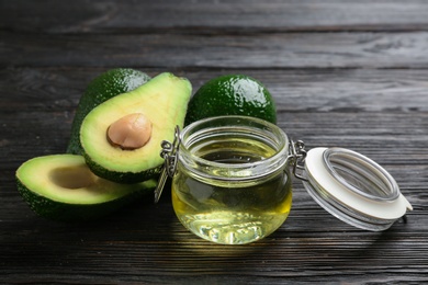 Photo of Jar of natural oil and avocados on dark wooden background