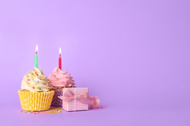 Birthday cupcakes with burning candles and gift box on violet background. space for text