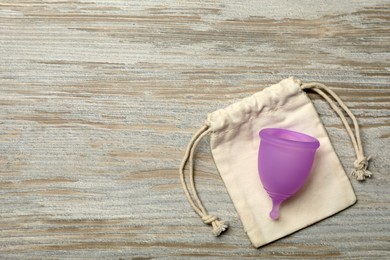 Photo of Menstrual cup with bag on light wooden background, top view. Space for text