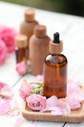 Photo of Rose essential oil and flowers on white wooden table