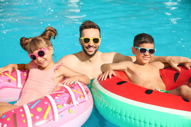 Photo of Father and children with inflatable rings in swimming pool. Family vacation