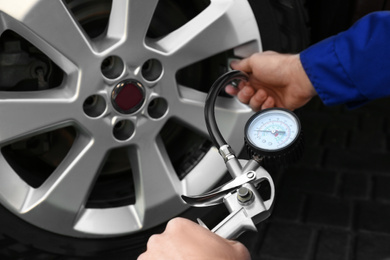 Photo of Mechanic checking tire air pressure at car service, closeup