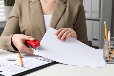 Photo of Woman stapling papers at white table indoors, closeup