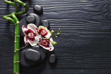 Photo of Spa stones with orchid flowers and bamboo on dark wooden background, top view. Space for text