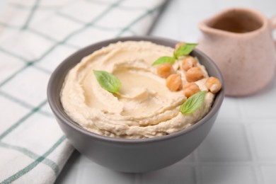Photo of Delicious hummus with chickpeas served on white tiled table, closeup