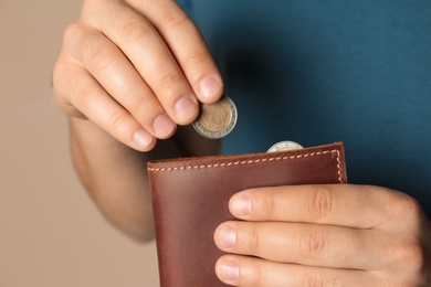 Photo of Young man putting coin into wallet on beige background, closeup