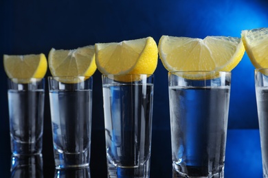 Photo of Shot glasses of vodka with lemon slices on dark blue background