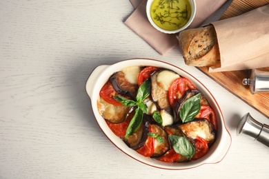 Flat lay composition with baked eggplant, tomatoes and basil in dishware on wooden table