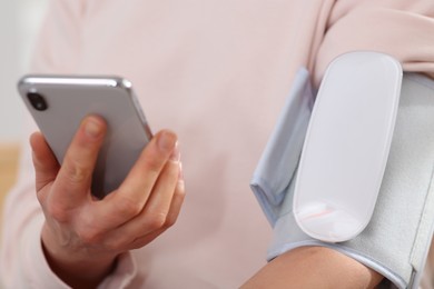 Photo of Woman checking blood pressure with modern monitor and smartphone indoors, closeup