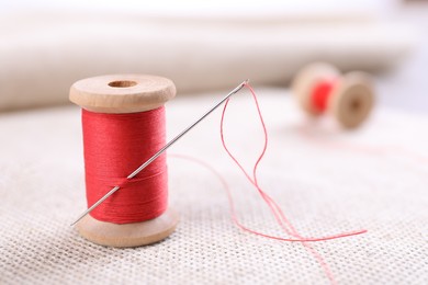 Photo of Spool of red sewing thread with needle on white fabric, closeup
