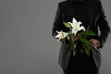 Photo of Man with white lilies on grey background, closeup and space for text. Funeral ceremony