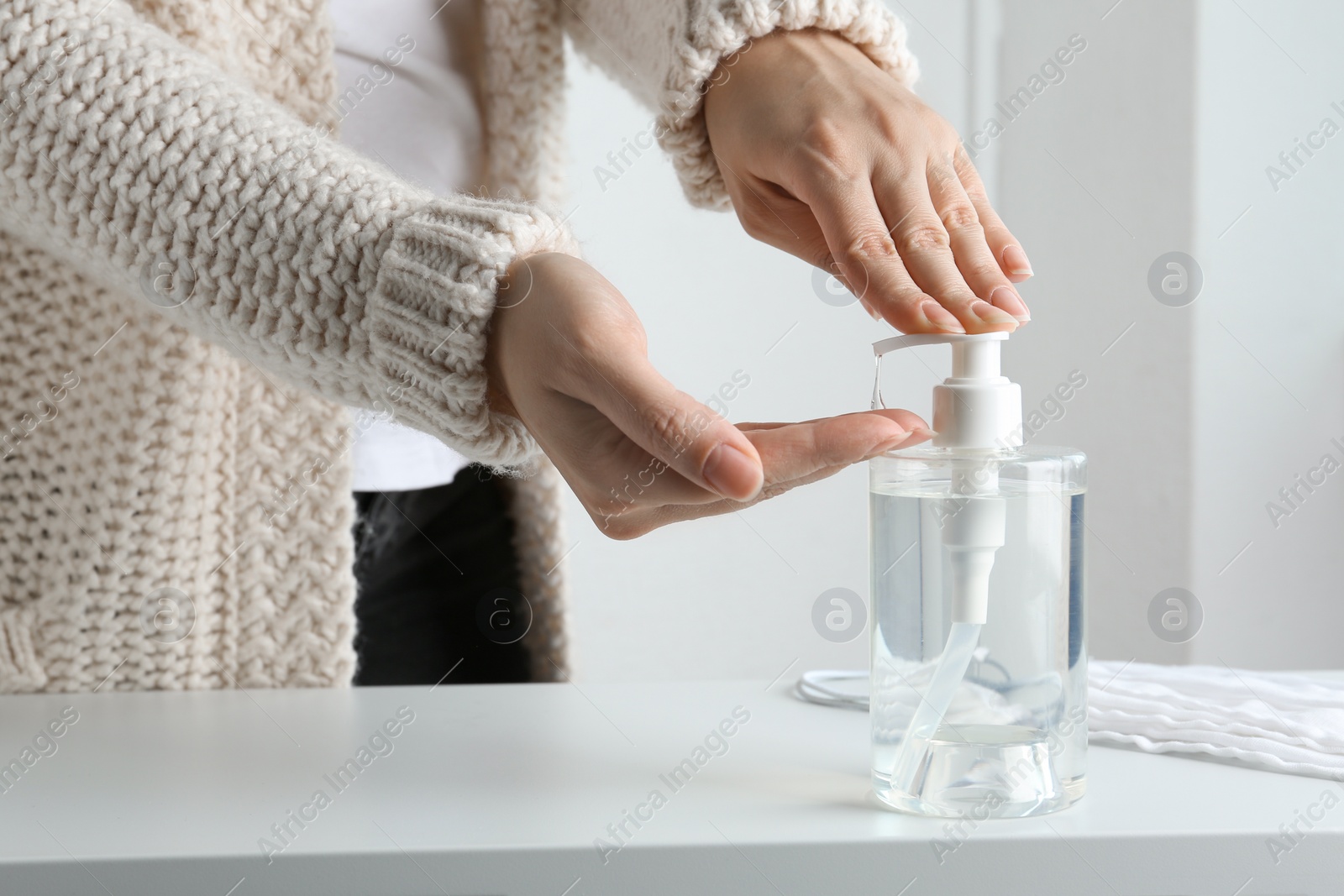 Photo of Woman applying antiseptic gel onto hand at table indoors, closeup. Virus prevention