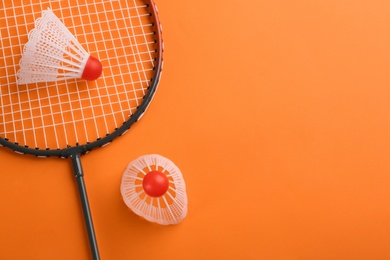 Photo of Badminton racket and shuttlecocks on orange background, flat lay. Space for text