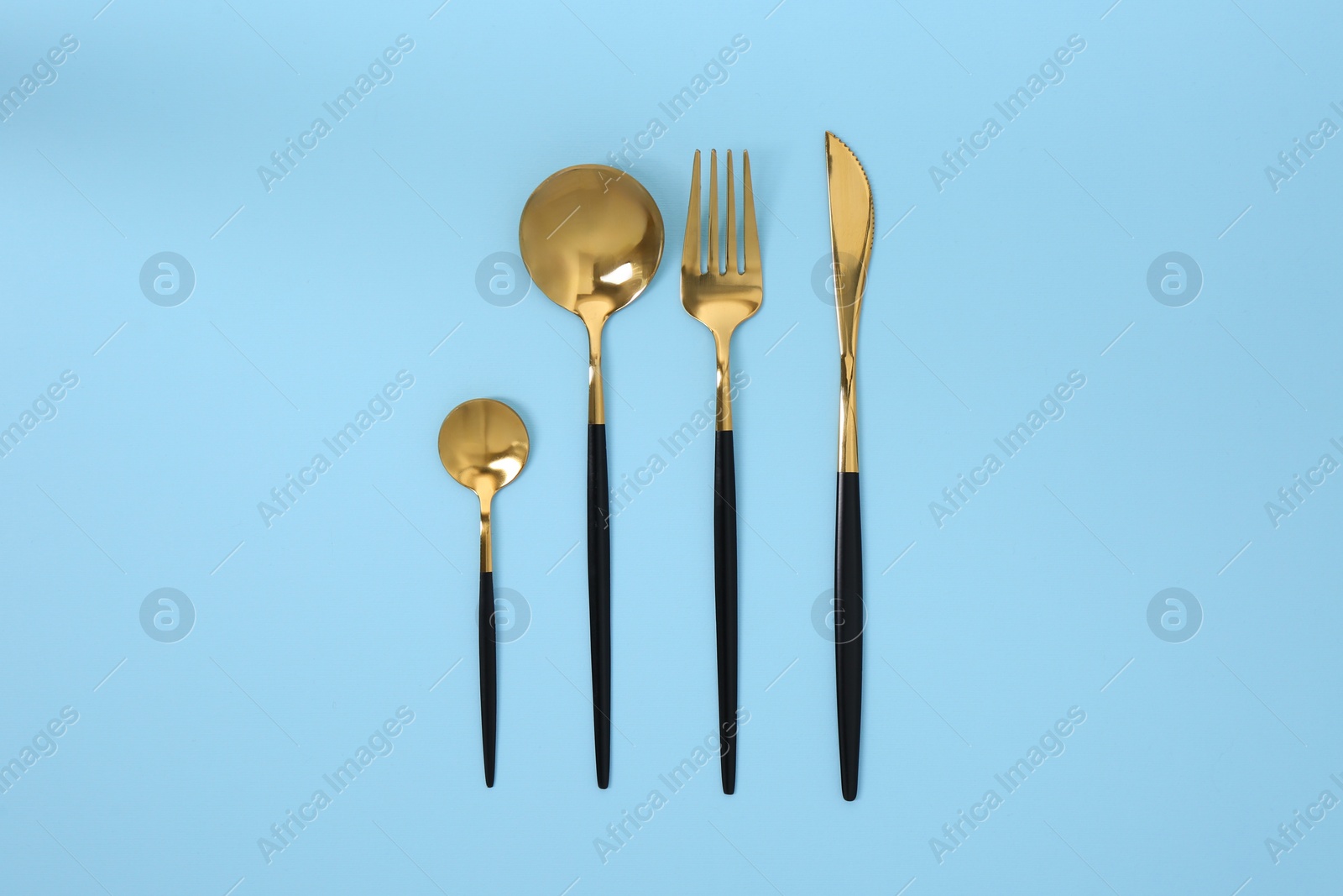 Stylish golden cutlery set on light blue background, flat lay Photo of Stylish golden cutlery set on light blue background, flat lay