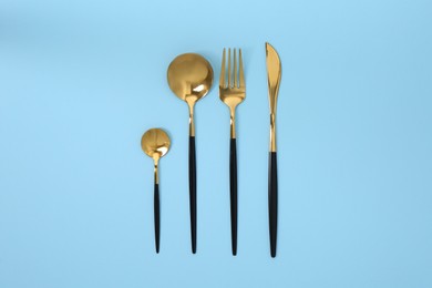 Photo of Stylish golden cutlery set on light blue background, flat lay