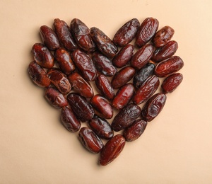 Photo of Heart shaped pile of sweet dried date fruits on color background, top view with space for text