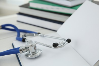 Photo of One new medical stethoscope and books on white table, closeup