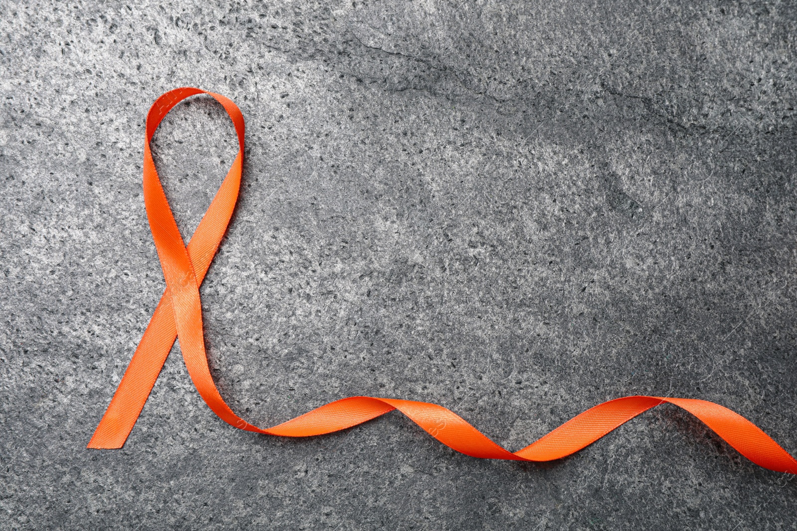 Photo of Orange ribbon on grey table, top view with space for text. Multiple sclerosis awareness