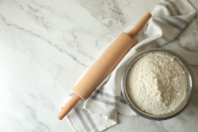 Photo of Flour in bowl, rolling pin and napkin on white marble table, top view. Space for text
