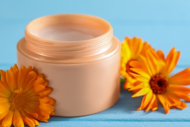 Photo of Jar of cream and beautiful calendula flowers on light blue wooden table, closeup