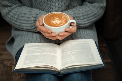 Photo of Woman with cup of coffee reading book at home, closeup