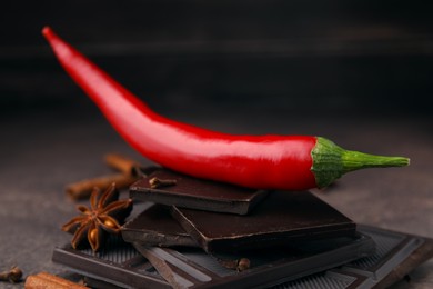 Photo of Delicious chocolate, fresh red chili pepper and spices on grey textured table, closeup