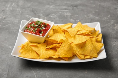 Photo of Plate with delicious mexican nachos chips and salsa sauce on grey table