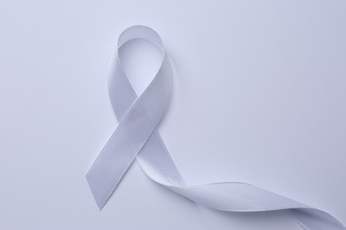 Photo of White awareness ribbon on white background, top view