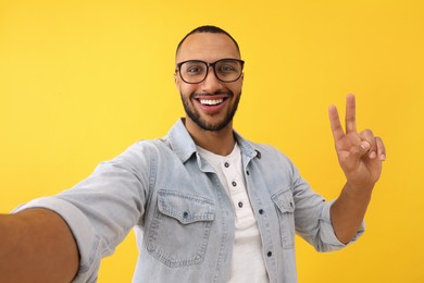Photo of Smiling young man taking selfie and showing peace sign on yellow background