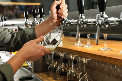 Photo of Bartender pouring fresh beer into glass in pub, closeup