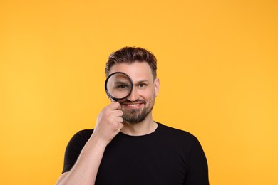 Photo of Happy man looking through magnifier on yellow background