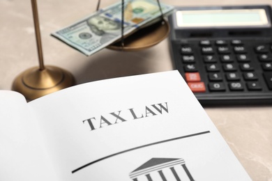 Photo of Scales of justice, money and book with words TAX LAW on table, closeup
