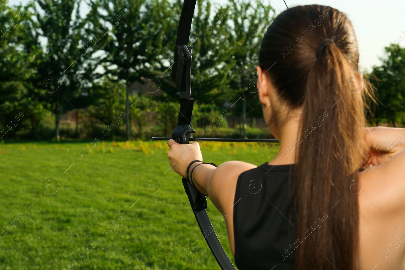 Photo of Woman with bow and arrow practicing archery in park, back view