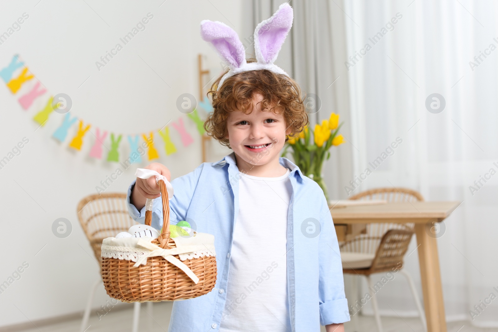 Photo of Happy boy in cute bunny ears headband holding Easter basket at home