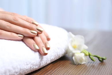 Photo of Woman with gold manicure on rolled towel at table, closeup. Nail polish trends