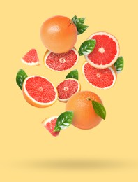 Image of Tasty ripe grapefruits and green leaves falling on beige background