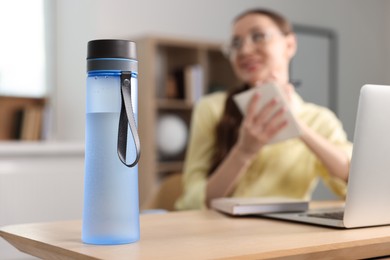 Photo of Woman working at wooden desk indoors, focus on bottle. Space for text