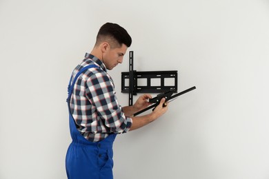 Photo of Professional technician with screwdriver installing TV bracket on wall indoors
