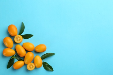 Photo of Fresh ripe kumquats with green leaves on light blue background, flat lay. Space for text