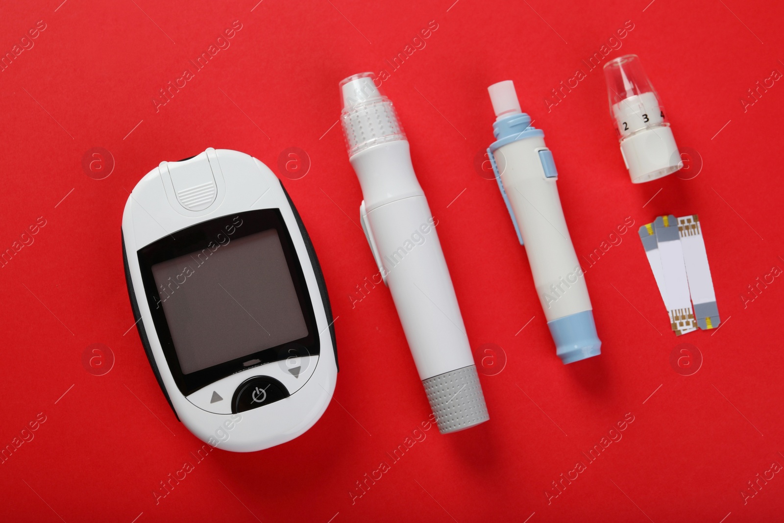 Photo of Digital glucometer, lancet pens and test strips on red background, flat lay. Diabetes control