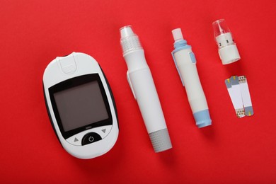 Photo of Digital glucometer, lancet pens and test strips on red background, flat lay. Diabetes control
