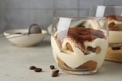 Photo of Delicious tiramisu in glass and scattered coffee beans on light table, space for text