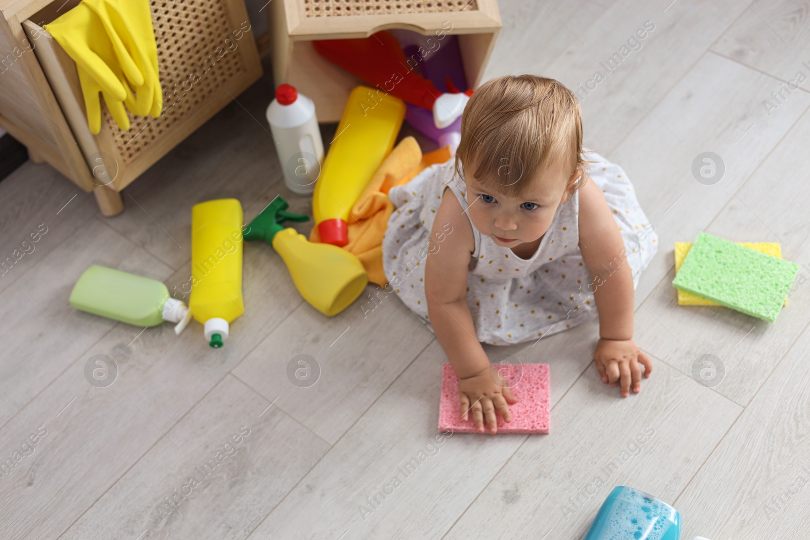 Photo of Cute baby playing with cleaning supplies on floor at home, above view. Dangerous situation