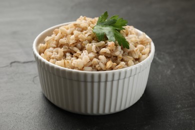 Photo of Tasty pearl barley porridge in bowl on dark textured table, closeup