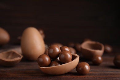 Half of tasty chocolate egg with candies on wooden table, closeup. Space for text