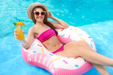 Photo of Young woman with cocktail in pool on sunny day